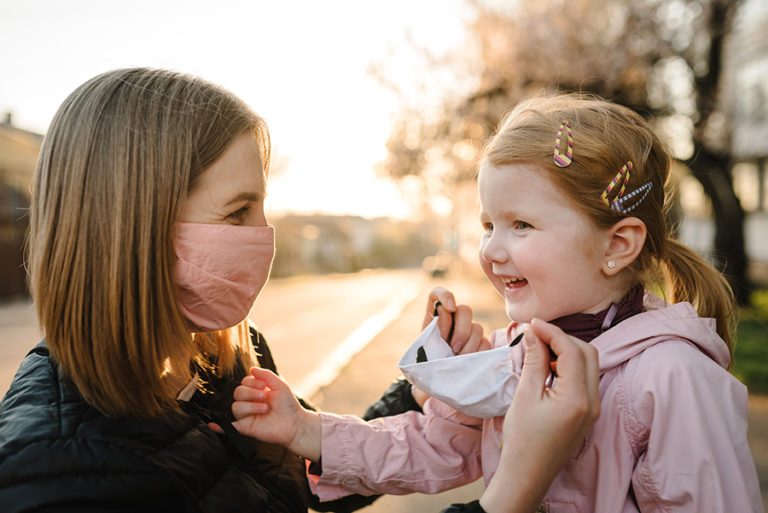 Mother helping her daughter put on a safety mask.